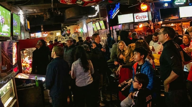 A crowded, dimly lit sports bar with multiple TVs showing a game and people socializing.
