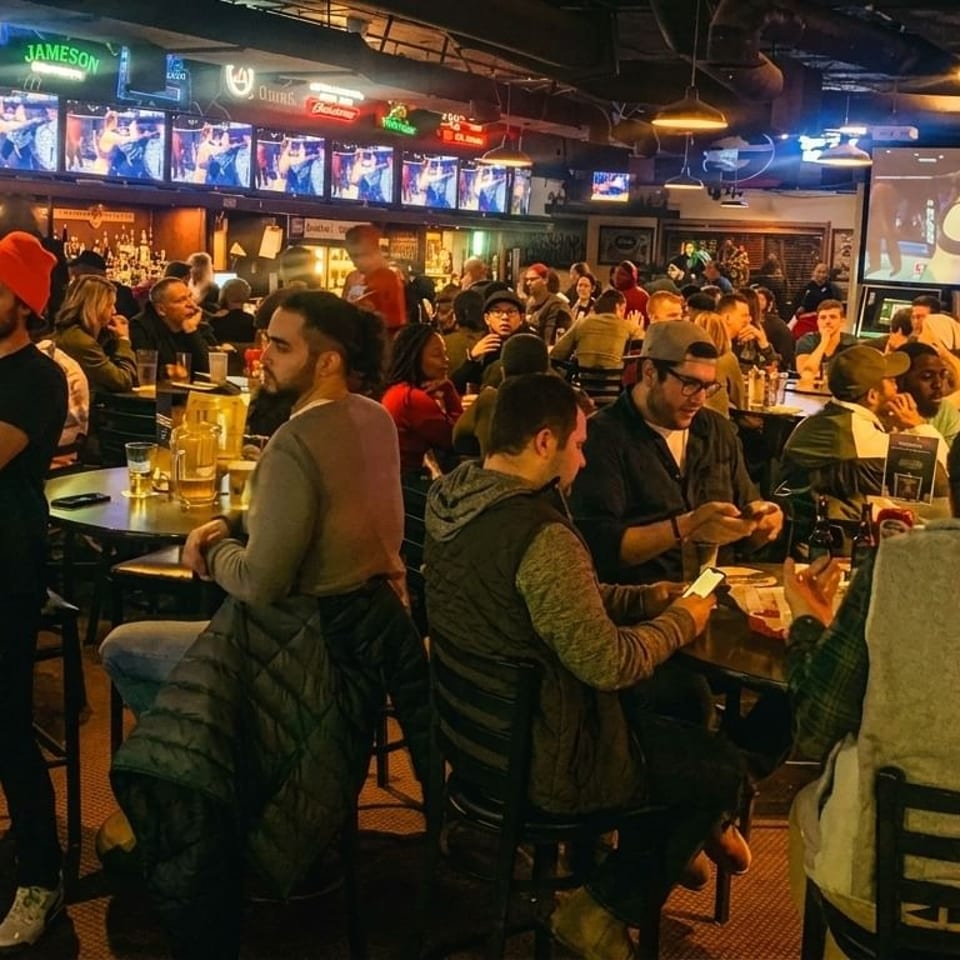 A lively sports bar with many patrons watching fights on multiple screens and socializing.