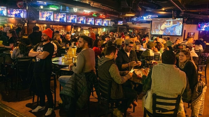A lively sports bar with many patrons watching fights on multiple screens and socializing.