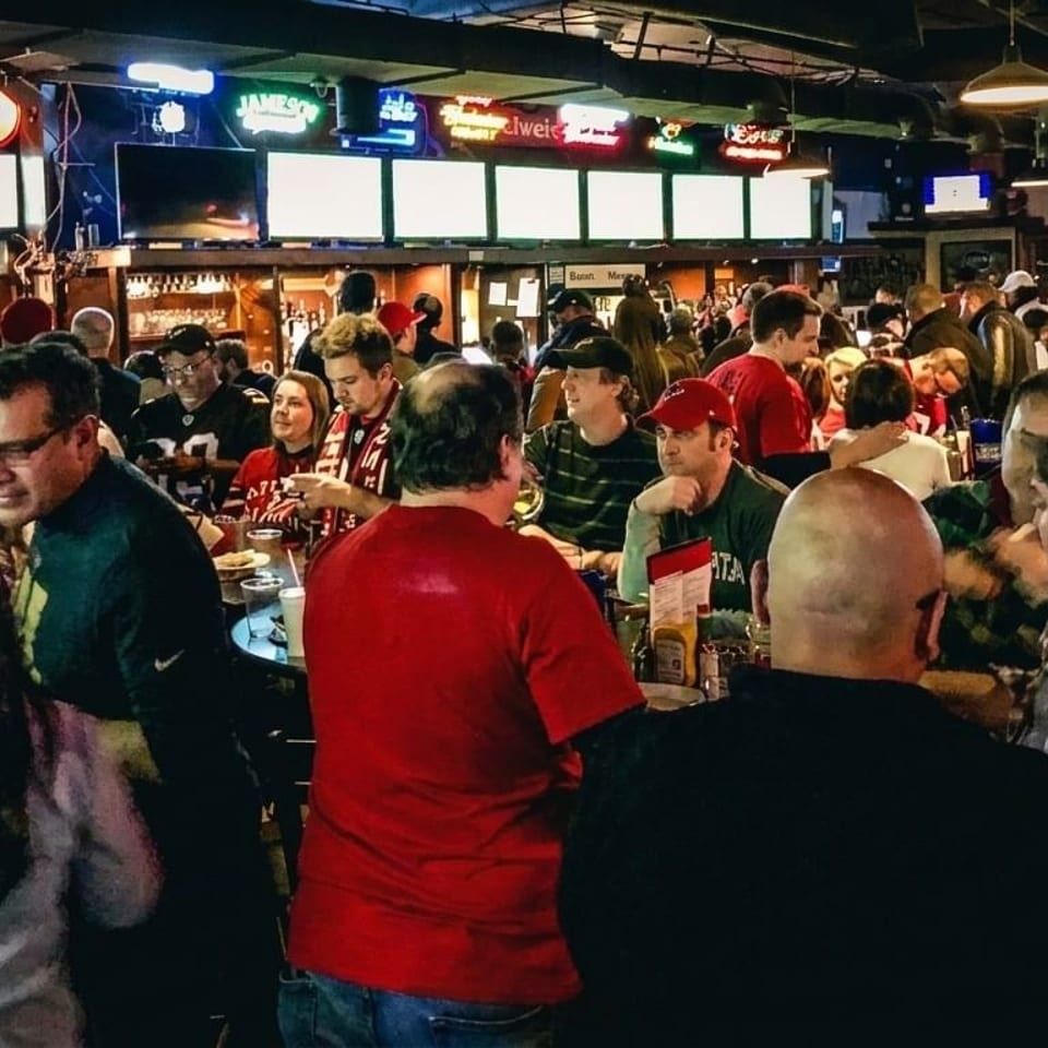 A lively, crowded sports bar with patrons socializing and watching games on multiple screens.