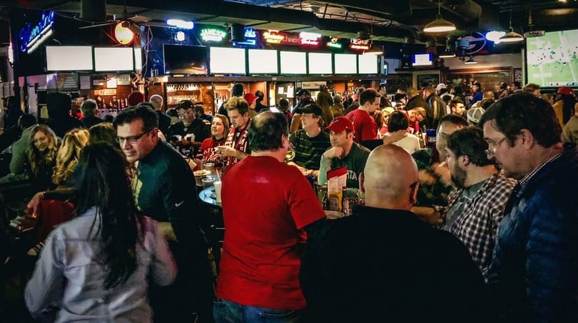 A lively, crowded sports bar with patrons socializing and watching games on multiple screens.